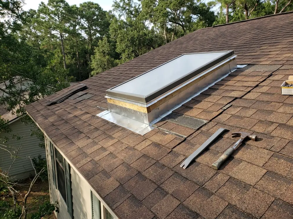 Step flashing kit fitted around a raised wood curb skylight on a shingle roof