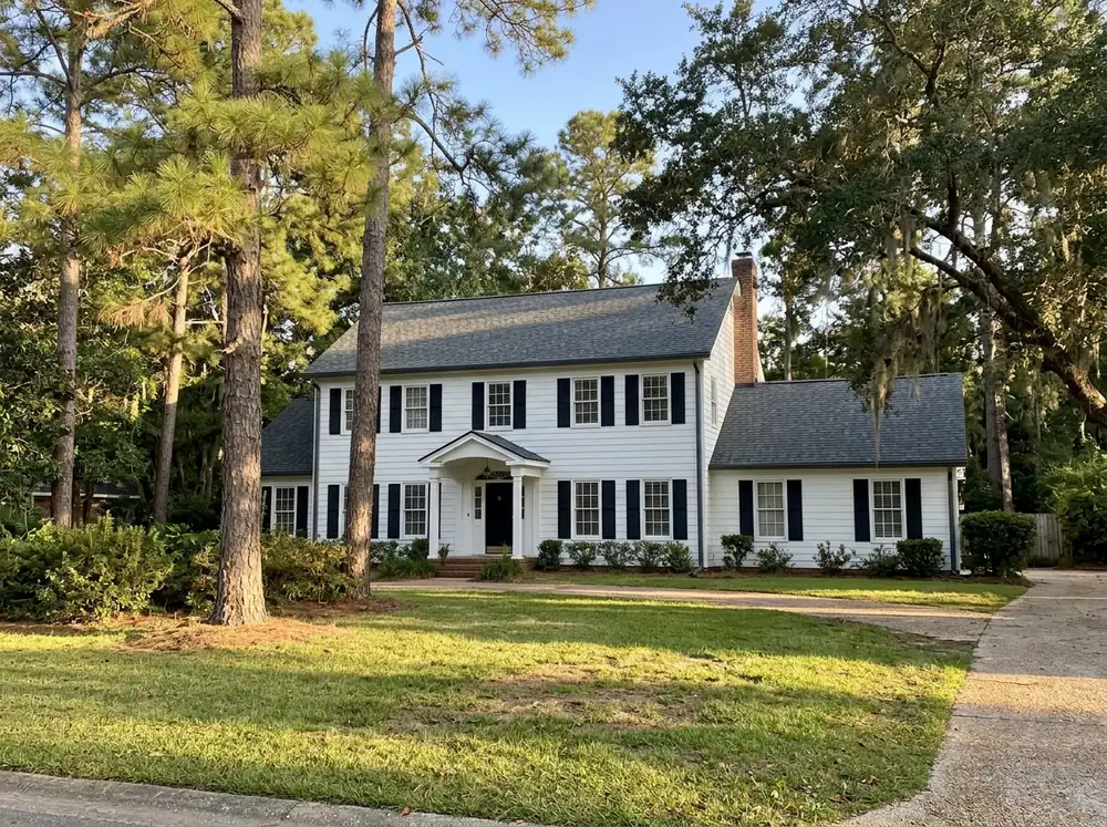 Two-story painted colonial house with a new dark gray impact-rated architectural shingle roof and pines behind it