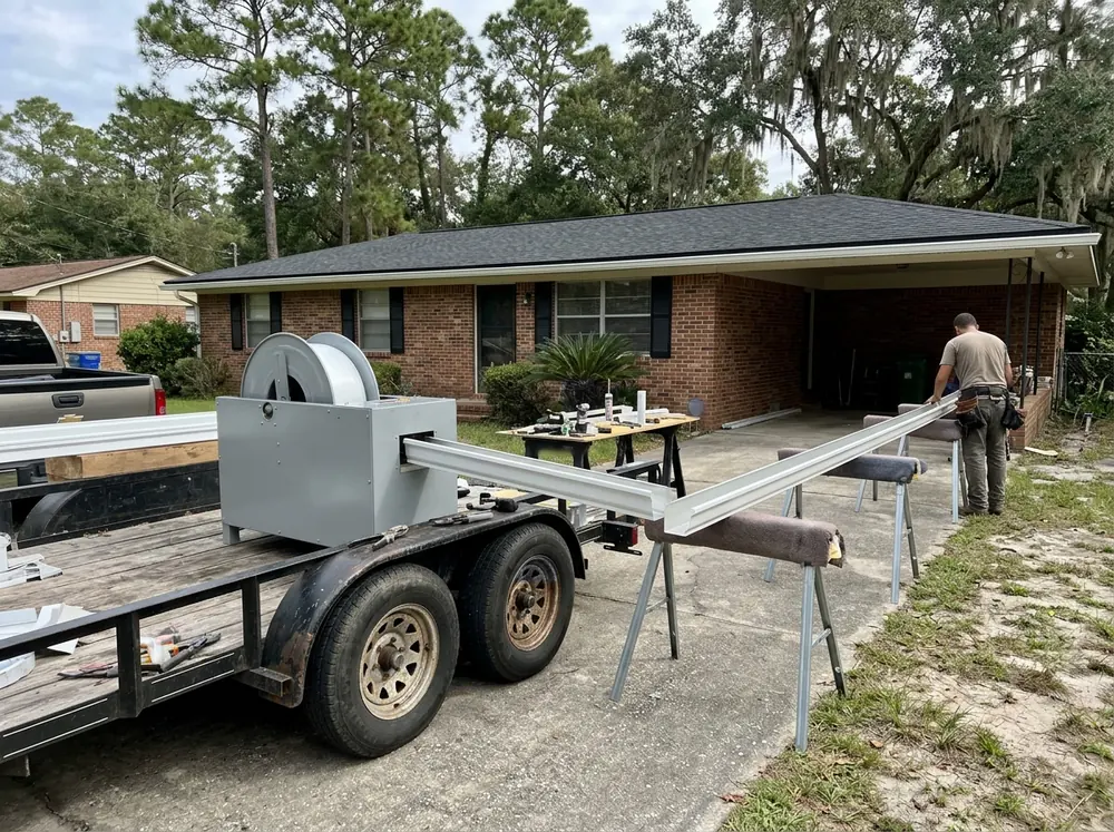 Gutter installer feeding aluminum coil through a portable seamless gutter machine on a trailer, a long K-style run coming out the other end